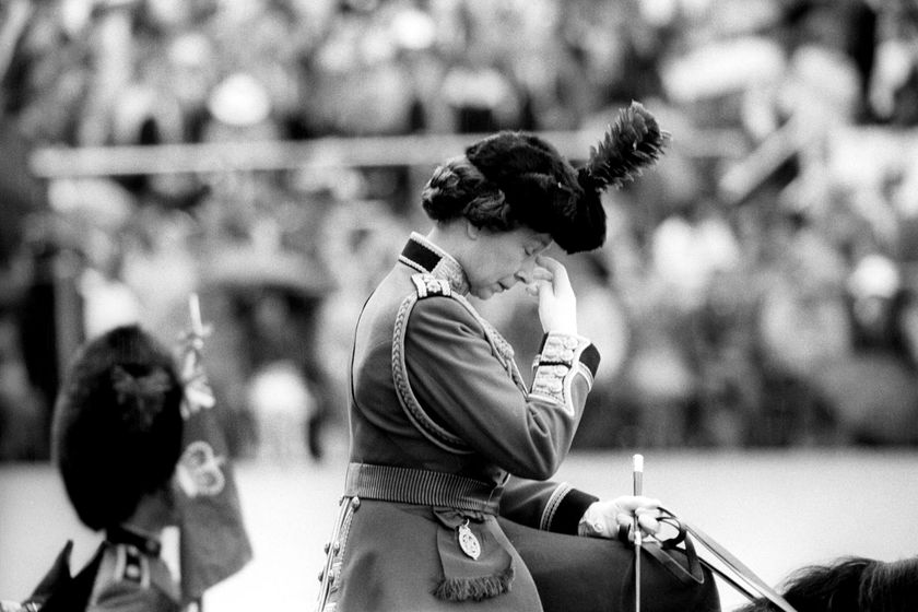 A uniformed woman on horseback wipes her face with her hand during The Queen's Platinum Jubilee, with a blurred crowd in the background. The image is in black and white.