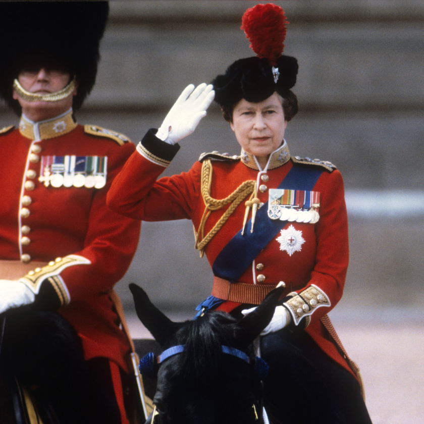 A woman in a red military uniform and black hat with a red plume salutes whilst riding a black horse, accompanied by another uniformed individual, during The Queen's Platinum Jubilee ceremony.