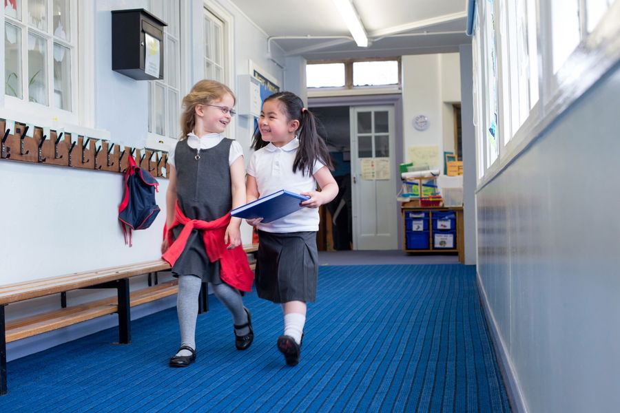 Two female nursery students walking together down the corridor. One is holding a book and they are both laughing in conversation.