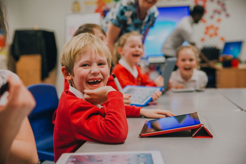 Happy little boy is smiling for the camera while using a digital tablet in his technology lesson at school.