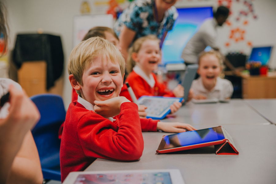 Happy little boy is smiling for the camera while using a digital tablet in his technology lesson at school.