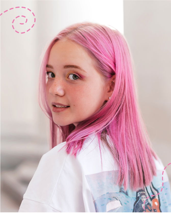 A young person with light skin and straight, pastel pink hair looks over their shoulder, wearing a white shirt with a colourful graphic. Pink doodle spirals are drawn near their head. The background is softly blurred.