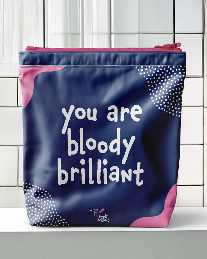 A navy blue pouch with pink and white accents and the text you are bloody brilliant printed on the front, placed on a white surface against a tiled wall background.