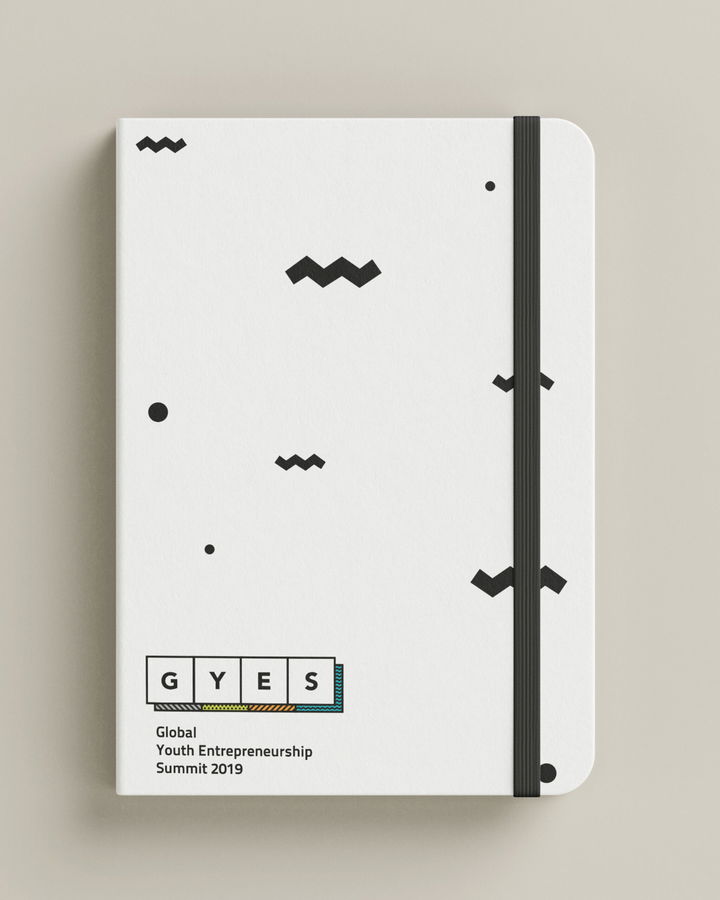 A white notebook with a black elastic band features scattered geometric shapes and the text GYES Global Youth Entrepreneurship Summit 2019 printed at the bottom left corner.