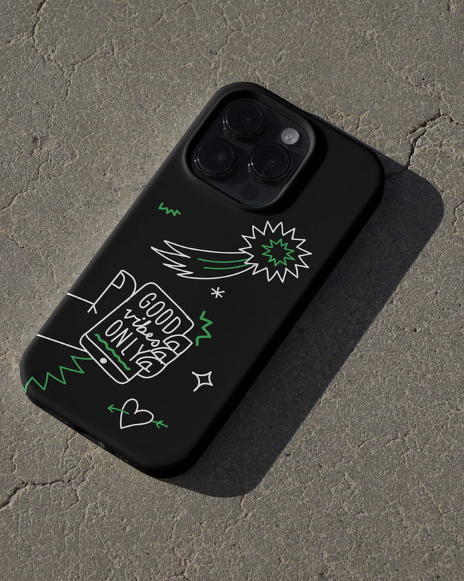 A black mobile phone case with white and green doodles, including a shooting star, heart, and the phrase Good Vibes Only, lying on a textured grey surface.