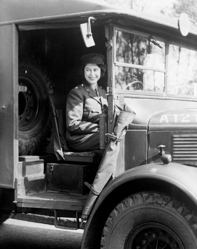 A woman in military uniform sits smiling in the driver’s seat of an old military vehicle, the door open and a spare tyre behind her. The black-and-white photo evokes memories celebrated during The Queen's Platinum Jubilee.