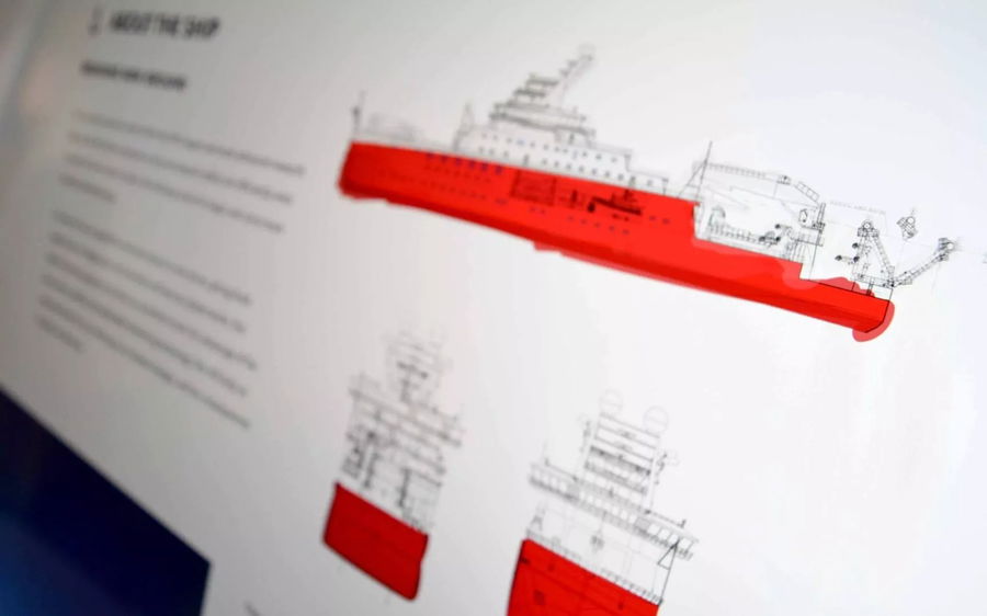 A close-up of a technical drawing showing the side and front views of a large ship, with the hull highlighted in red and descriptive text visible to the left of the diagrams.
