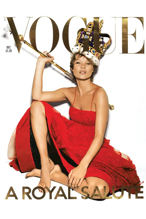 Model in a red dress sits barefoot on the floor, wearing a royal crown and holding a golden sceptre, celebrating The Queen’s Platinum Jubilee against a white background on the cover of Vogue magazine with the headline “A Royal Salute.”.