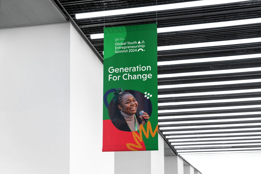 A large green banner hanging indoors reads Global Youth A.I. Entrepreneurship Summit 2024: Generation For Change and features a smiling young woman, colourful graphics, and modern design elements.