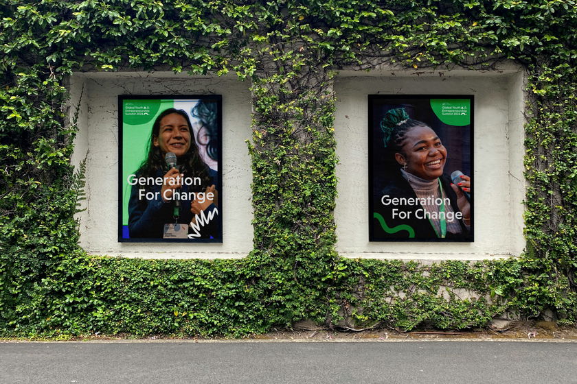 Two posters in window frames on an ivy-covered wall display smiling women with the text Generation For Change and the Global Shapers Community logo. The street is visible below the wall.